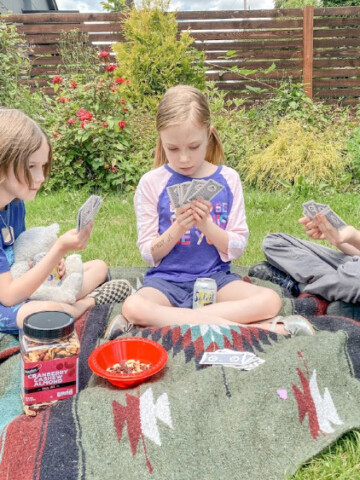 kids playing cards sitting on a picnic blanket