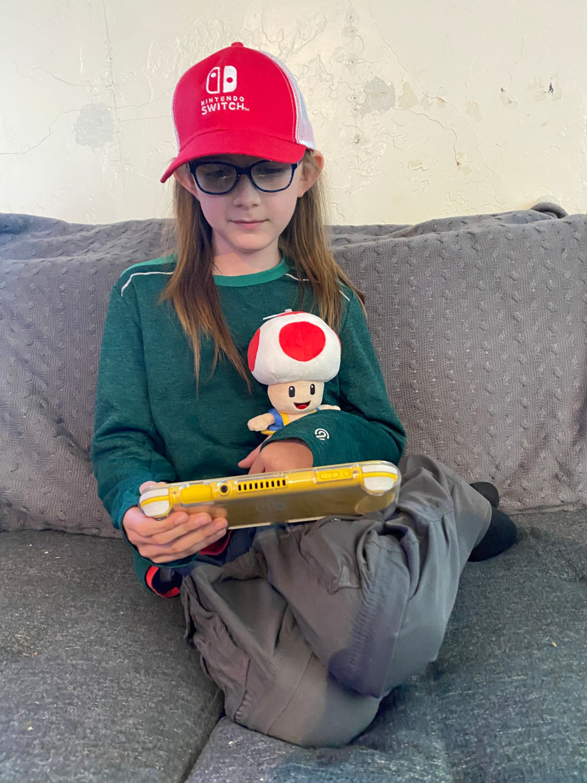boy in green shirt wearing a red hat playing a yellow nintendo switch