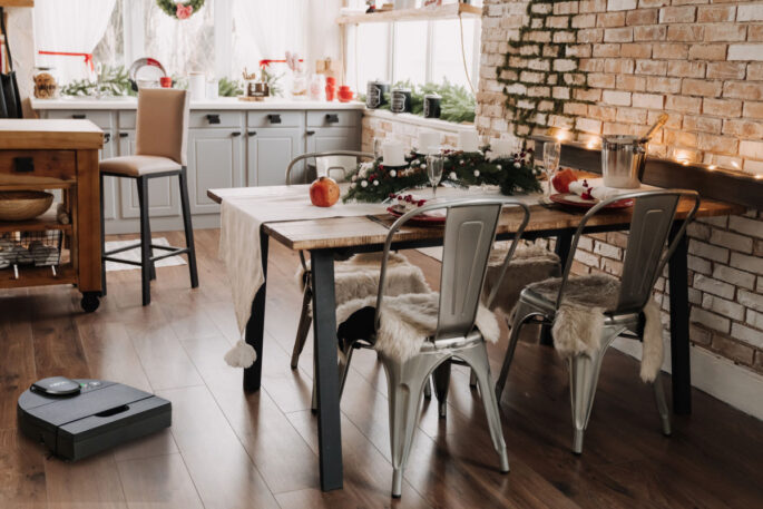 festive living space with table set with holiday decor, a robot vacuum is on the wood floor