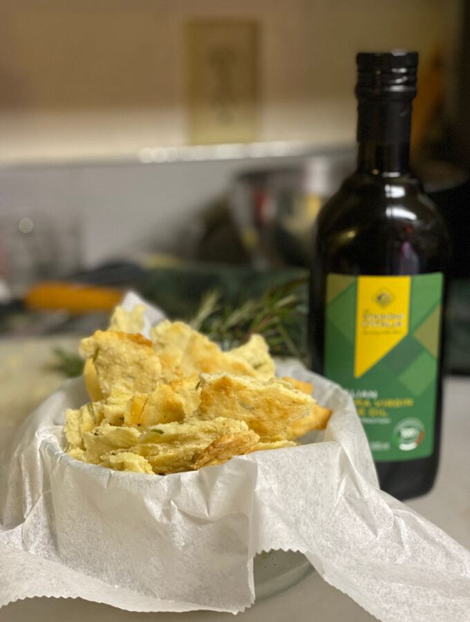 rosemary flatbread in a bowl with parchment paper and a bottle of extra virgin olive oil